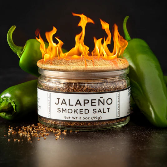 Jar of jalapeño smoked salt with flames and green peppers on a dark background